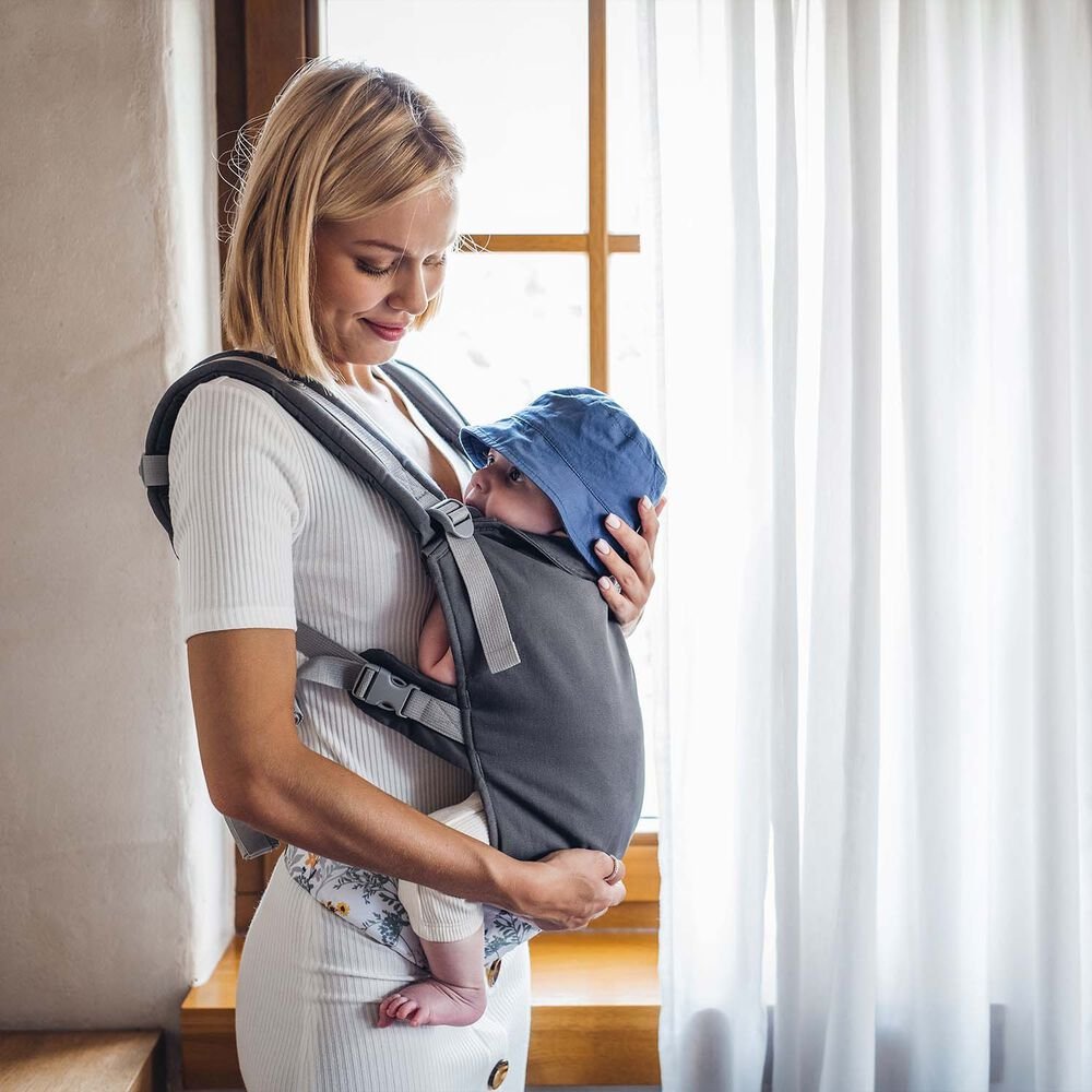 Zdjęcie poglądowe opiekunki z dzieckiem w nosidle MoMi COLLET Flowers przy oknie