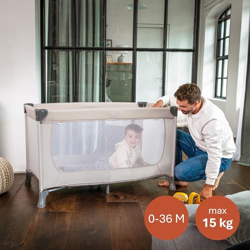 Dziecko w beżowym łóżeczku Hauck Dream N Play, z mężczyzną stojącym obok.